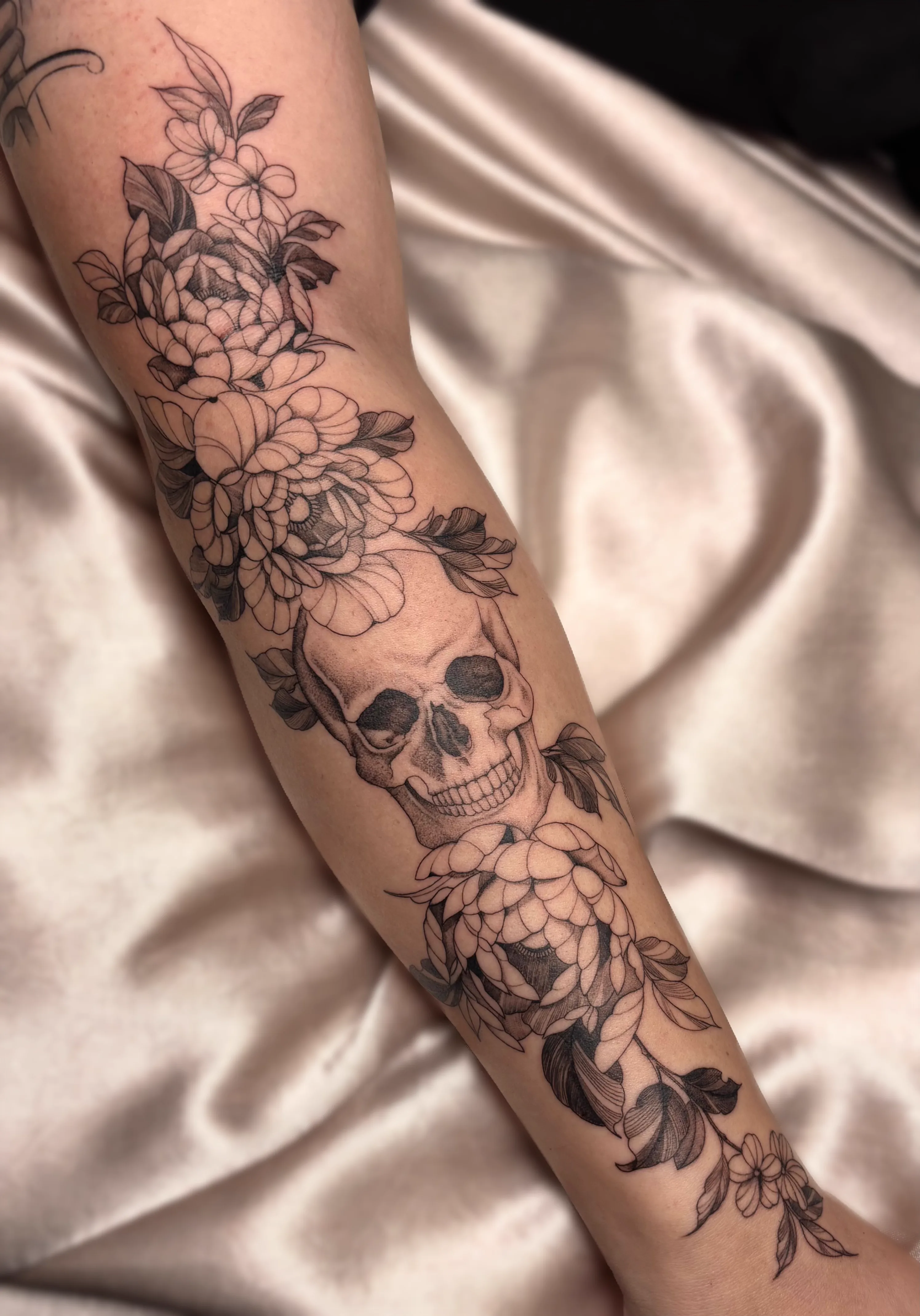 Tatuagem de caveira com composição floral no braço
