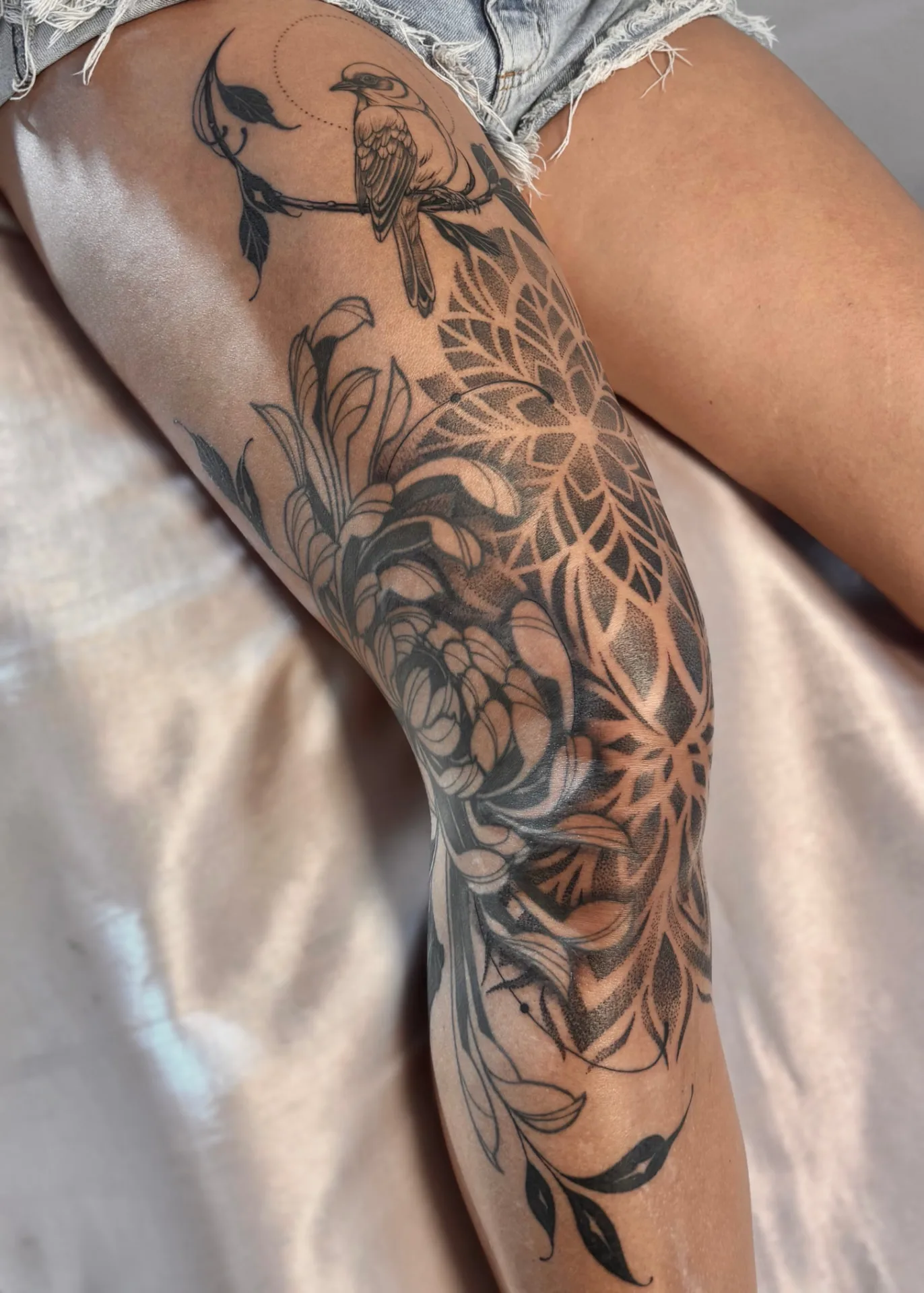 Tatuagem de pássaro com flores e mandala geométrica na perna
